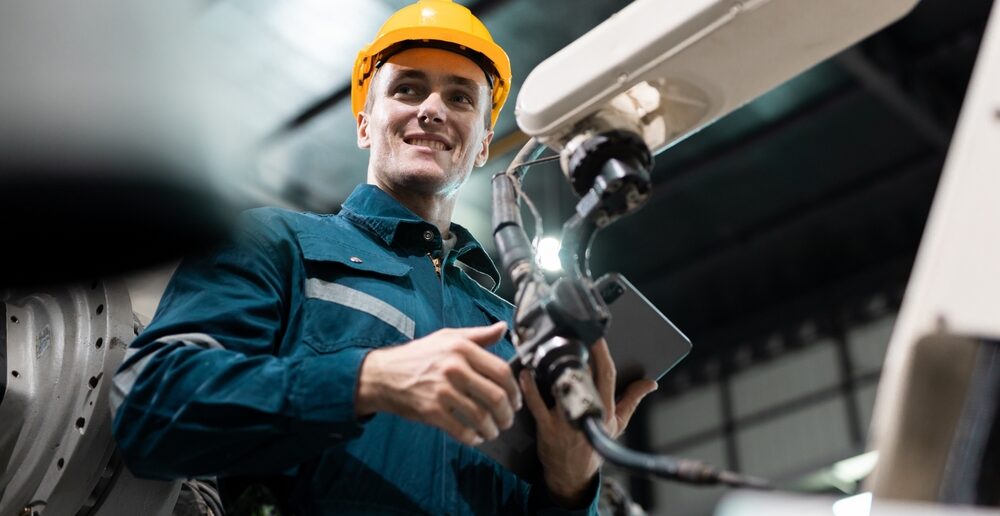 Uśmiechnięty pracownik zakładu produkcyjnego nadzoruje pracę robota